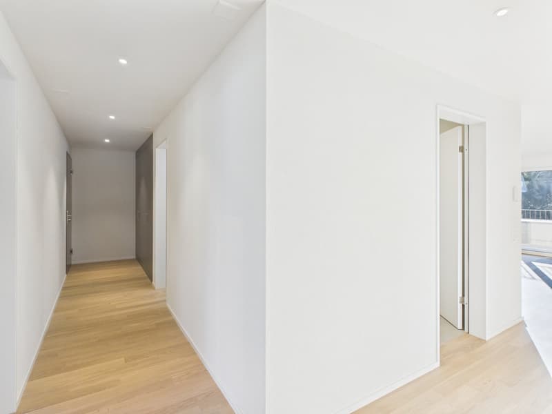 hallway with hardwood floors, white walls, light wooden doors, open balcony