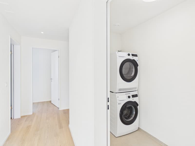 Utility room, white walls, wooden floor, white washer and dryer stacked