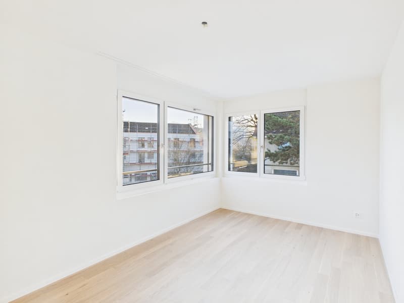 Empty room with three windows, white walls, and wooden floor.