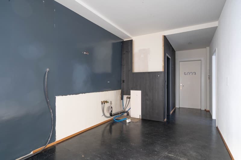 Unfinished room with gray walls, black floor, white ceiling, pipes and wires visible