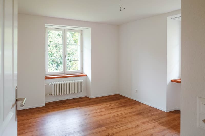 large room with hardwood floor, white walls, and glass window with view of the outside