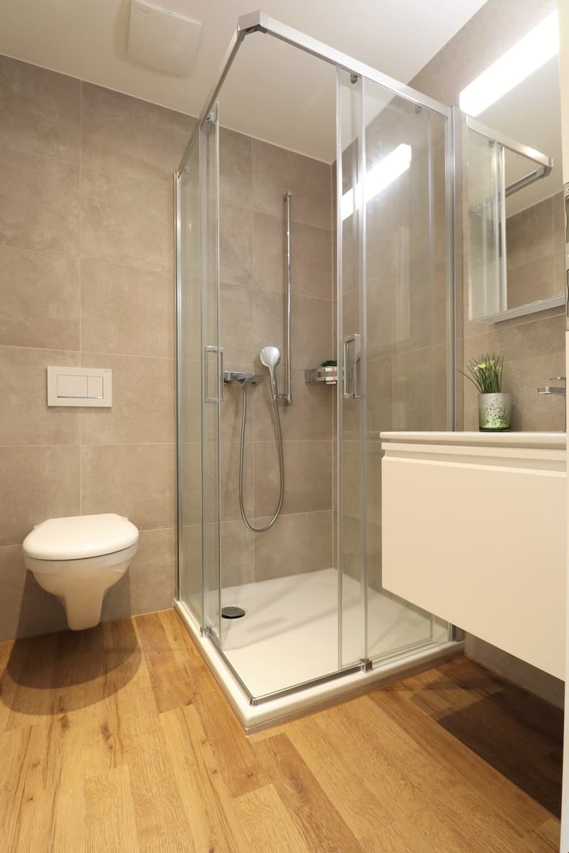 Bathroom with shower, toilet, wall-mounted soap holder, wooden floors, white tiles, light