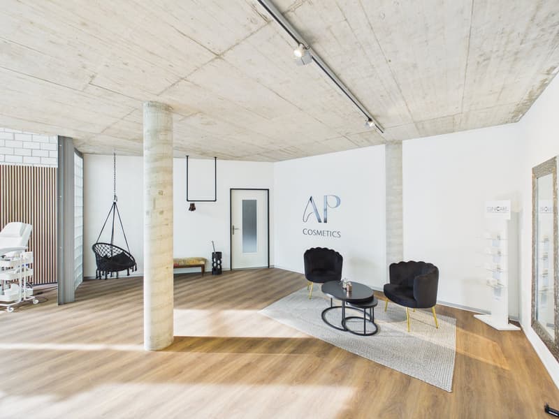 Bright room with wooden floors, black chairs, black round table, white walls, AP Cosmetics signage