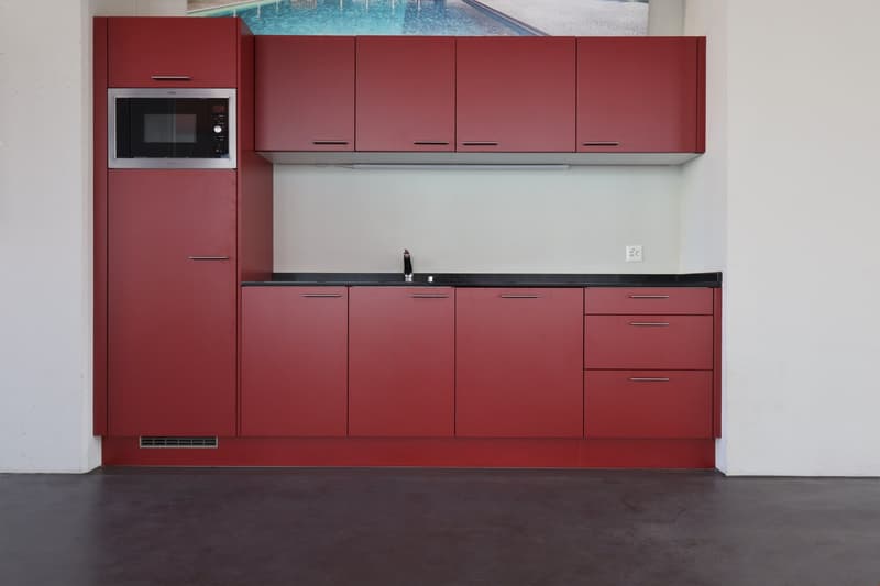 modern kitchen with red cabinets, black countertops, integrated microwave, sink with faucet, electrical outlet