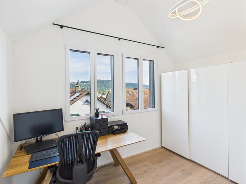 wooden desk, black office chair, computer monitor, printer, wooden floor, white walls, large windows