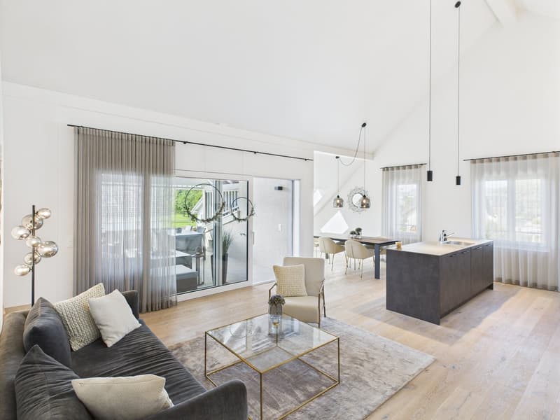 modern living room with large windows, glass doors, wooden floor, gray couch, glass coffee table, pendant lights, kitchen island, dining table, and chairs
