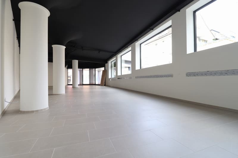 Empty room with white tiles, white pillars, black ceiling, large windows