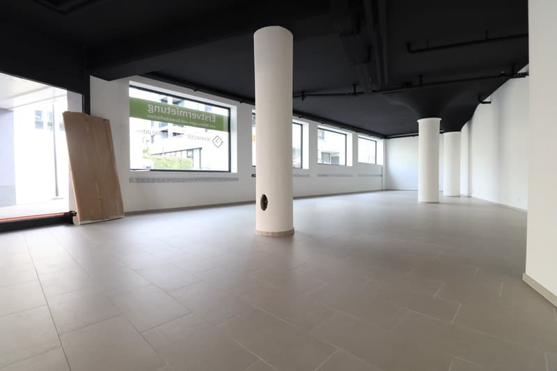 Empty room with tiled floor, white walls, large windows, and two central pillars.