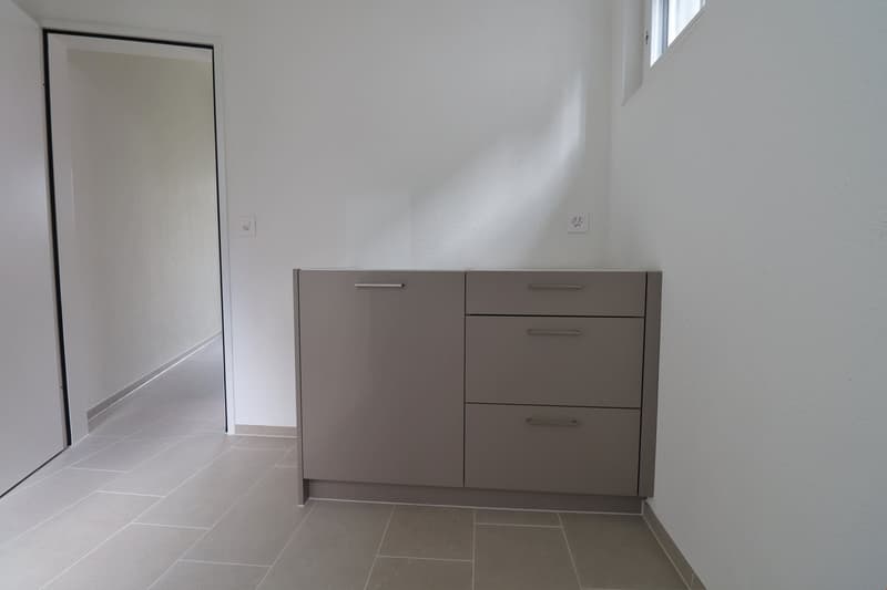 Empty room with white walls, tiled floor, gray cabinet with three drawers, power outlet on the wall