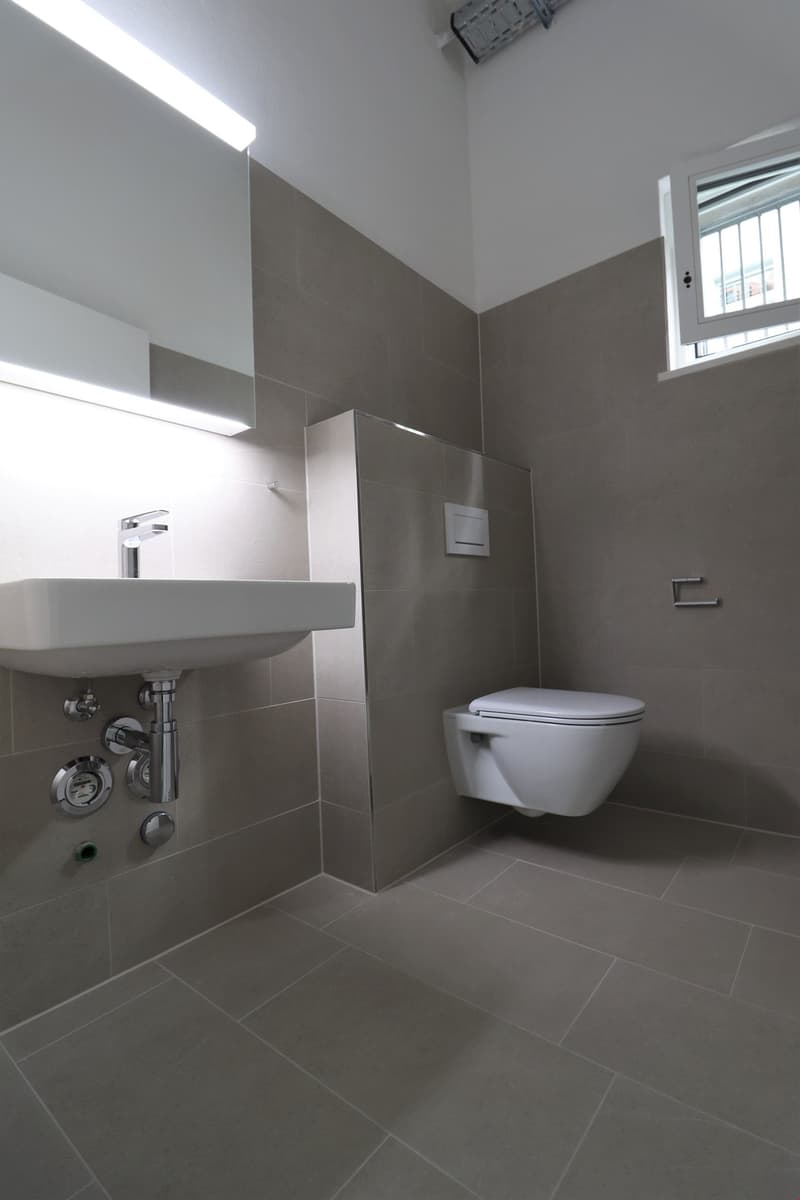 modern bathroom with white sink, silver faucet, white toilet, gray tiles, small window