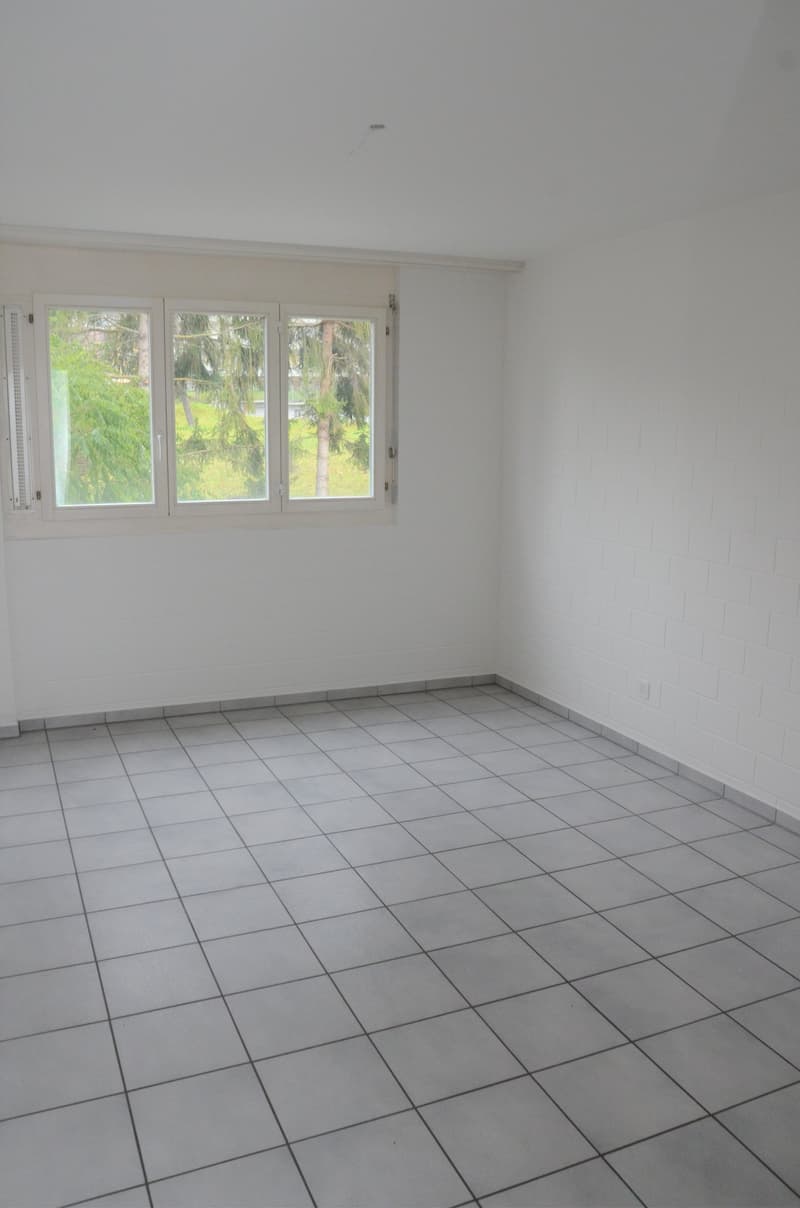 empty room, white walls, gray tile flooring, three windows, electrical outlet on right wall