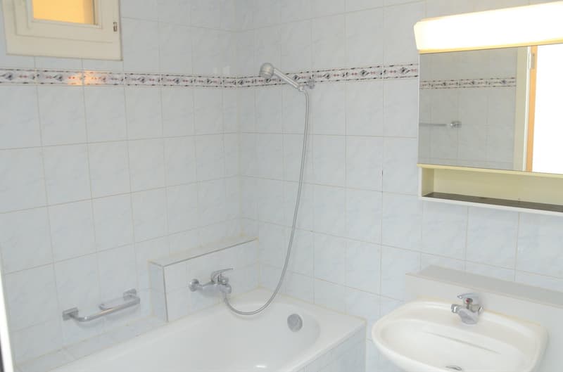 Bathtub with shower head, sink with faucet, mirror with light, tiled walls