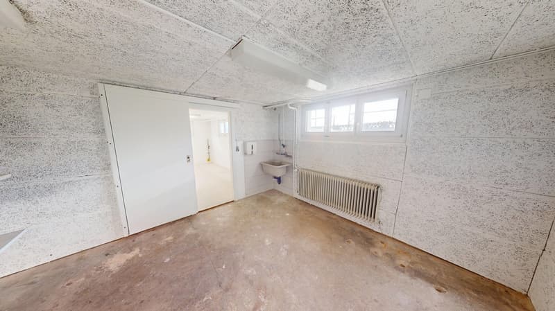 a single room with white walls, concrete floor, white door, sink, radiator and window