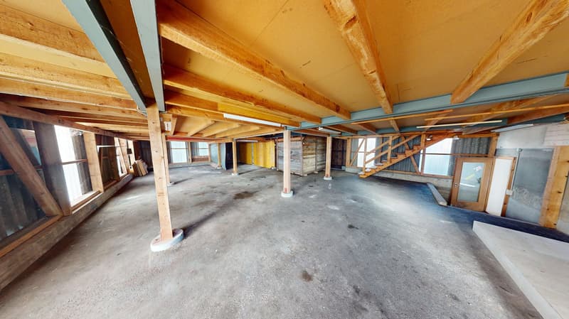 An empty room with wooden beams, concrete floor, and exposed ceiling, along with a staircase