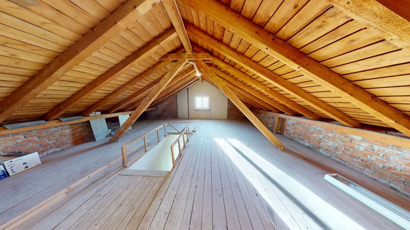 A large attic space with wooden flooring, wooden roof trusses, brick walls, and a window