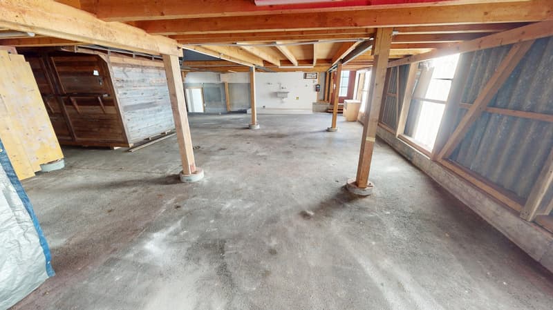 spacious room, concrete floor, wooden ceiling beams, multiple support columns, open layout, large windows, unfinished interior