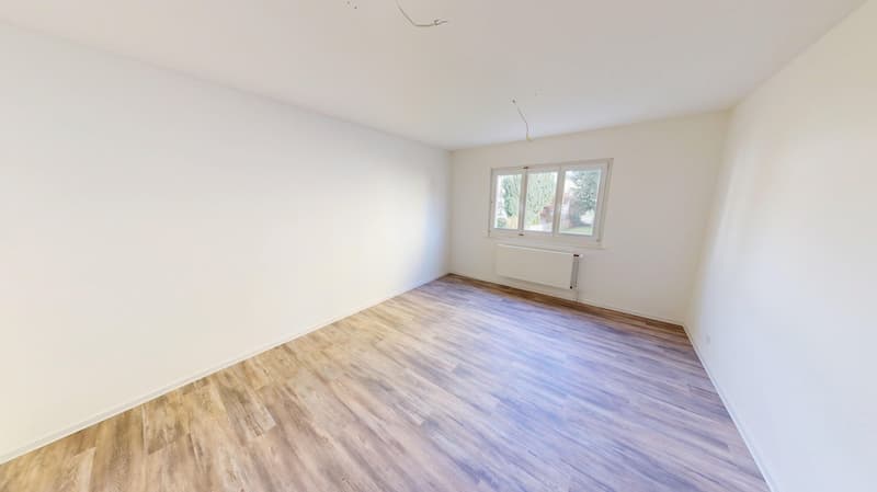 Empty room with white walls, wooden floor, a window, and a white radiator