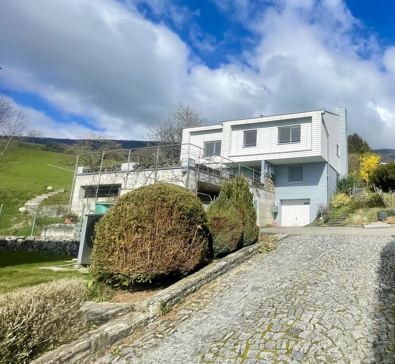 White house with balcony, garage, stone driveway, large garden with steps, green bushes