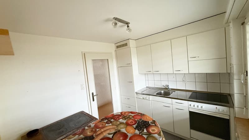 White kitchen cabinets, white tiled backsplash, stainless steel sink and dishwasher, electric range, wall-mounted lights, door to hallway, tiled floor