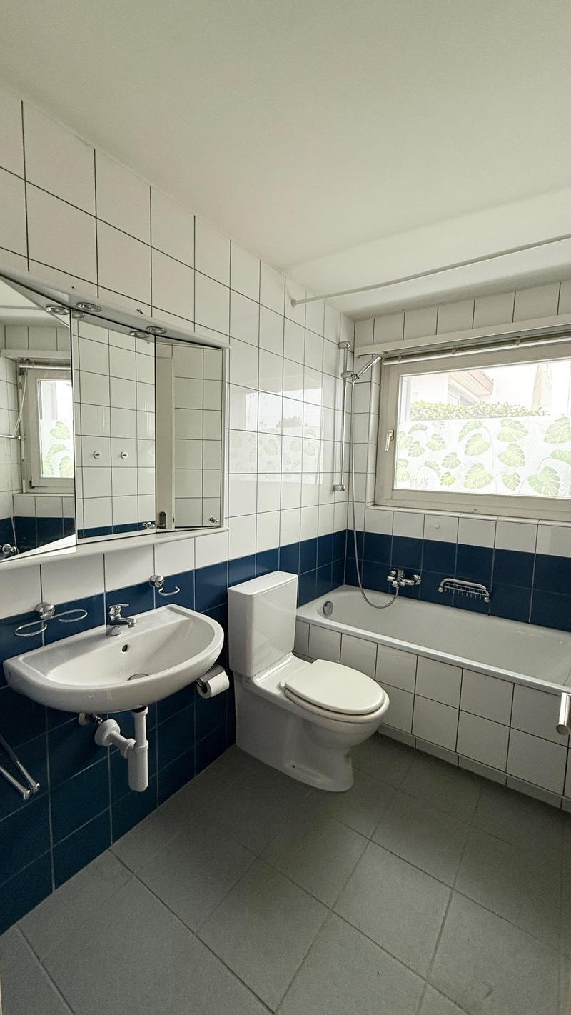 Tiled walls and floors, white sink with silver faucet, white toilet, bathtub, mirror, and towel bar
