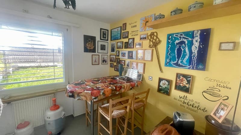 yellow walls, desk with chairs, table cloth, frames on the wall, radiator, trash bin, painting on the wall