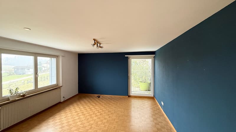 Empty room with wooden floors, blue walls, ceiling lights, and a window.