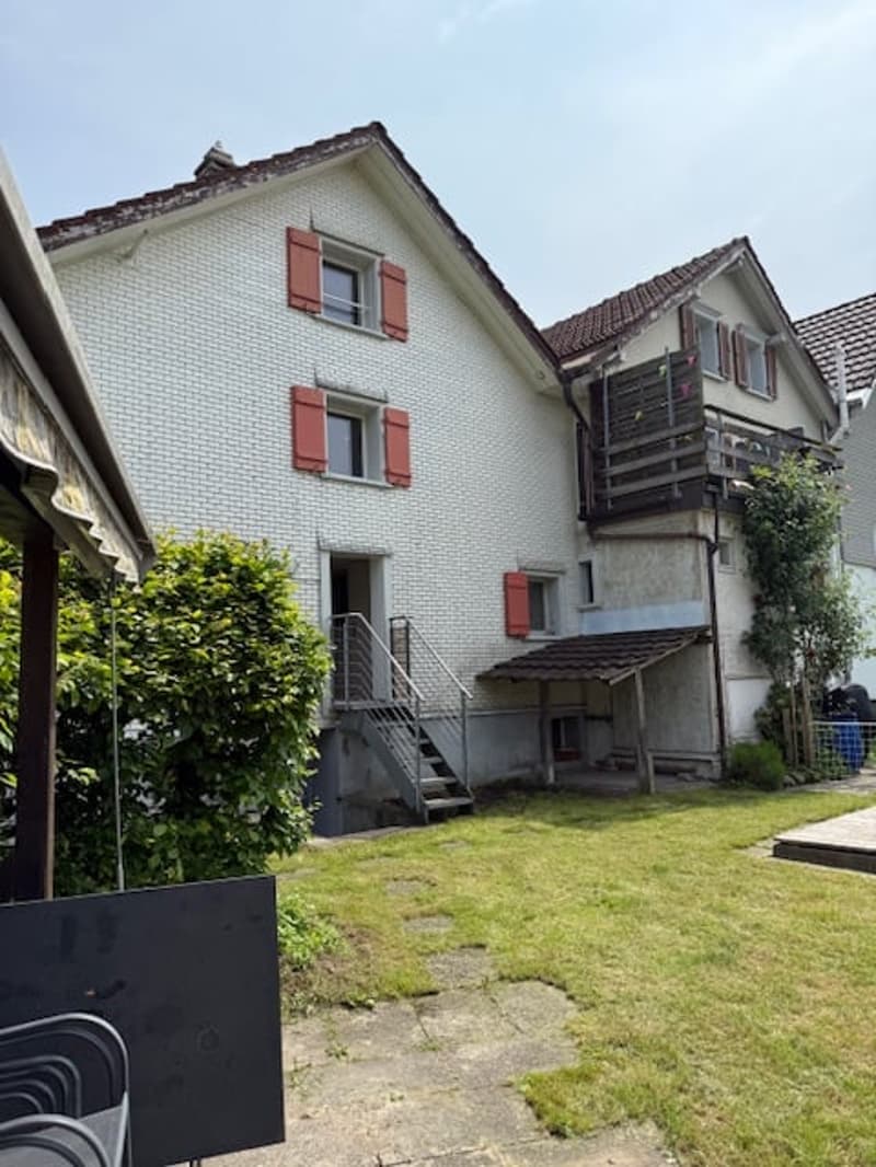 White house, red shutters, balcony, metal staircase, well-maintained garden