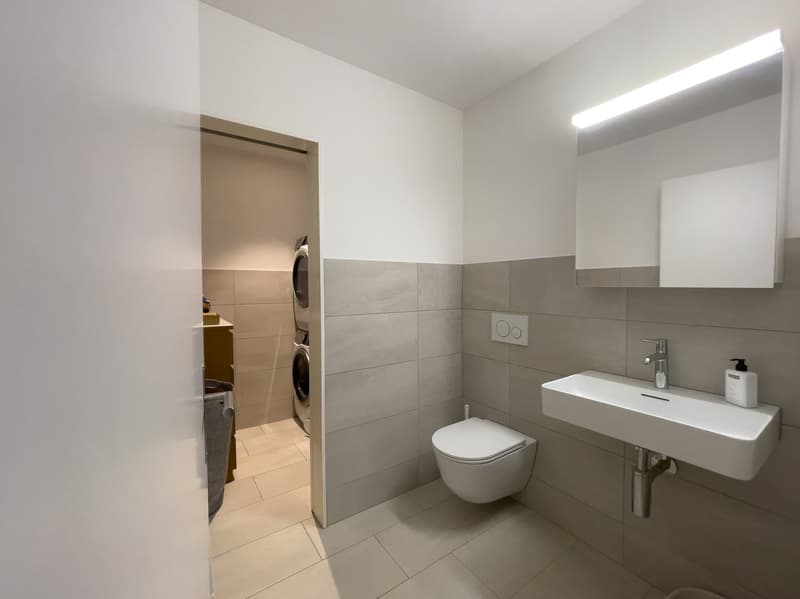 modern bathroom with white tiles, white sink, white toilet, washing machine, mirror, light