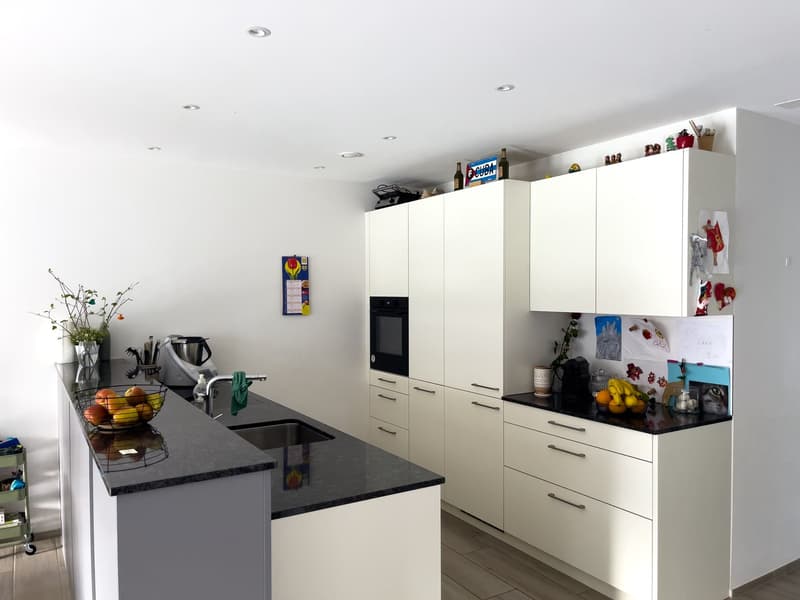 modern kitchen with white cabinets, black countertops, stainless steel sink, built-in oven, refrigerator, and various kitchen appliances
