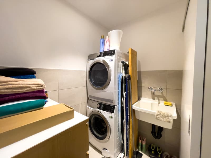 Laundry room with stacked washer and dryer, sink, and storage