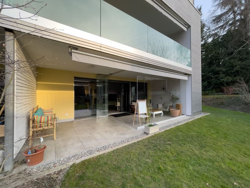 Modern house with glass walls, yellow exterior, large terrace, wooden furniture, potted plants, green lawn