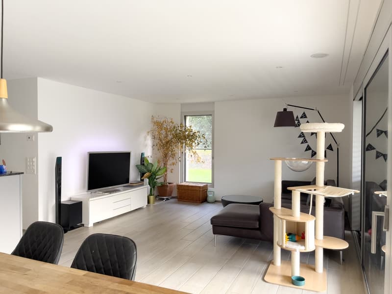 modern living room, white walls, wooden floor, white entertainment center, flat screen TV, speakers, potted plants, cat tree, couch, round coffee table, lamps