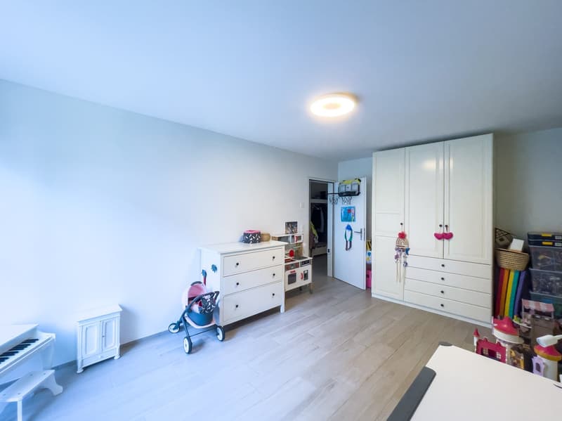 A room with white walls, wooden floor, white cabinets, a white piano, a stroller, and a white stool.