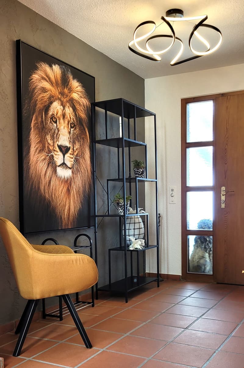 Entrance: lion painting, dark chair, shelf with plants and bowl, modern lamp, wooden door