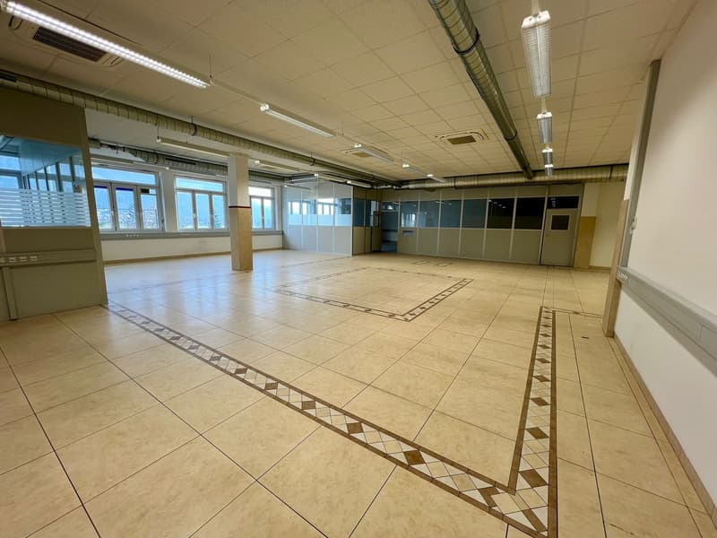 Large open office space with tile flooring, suspended ceiling, and windows along the walls. The room appears to be empty and ready for use.