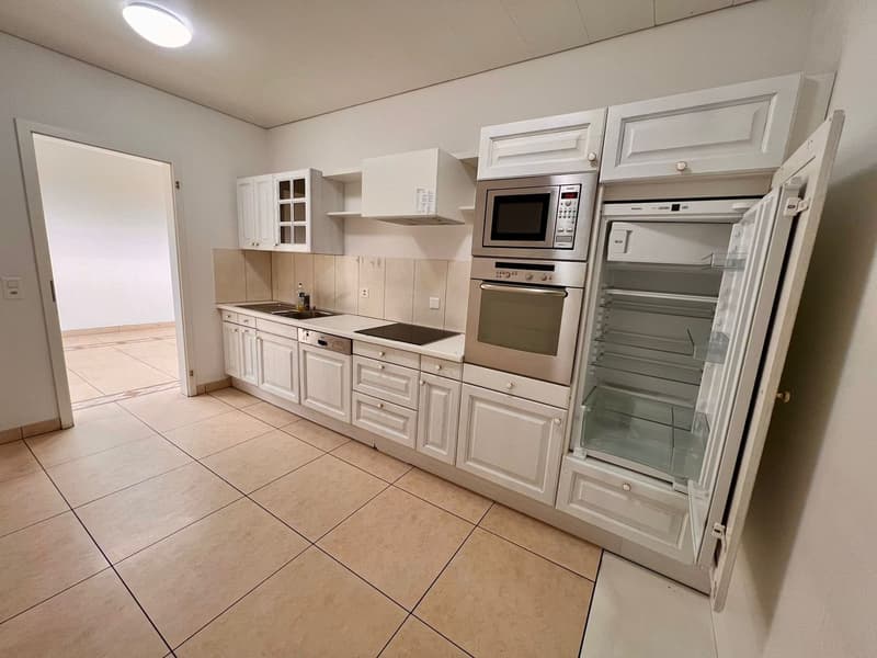 Spacious kitchen with white cabinets, stainless steel appliances including a refrigerator and dishwasher, tile flooring, and ample counter space.