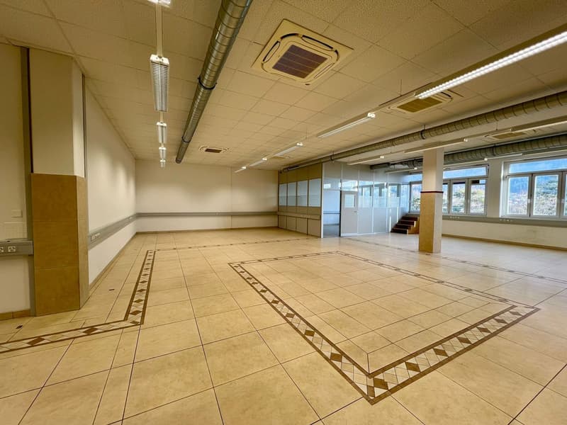 Large open commercial space with beige tile flooring, recessed lighting, and air conditioning units in the ceiling. The space appears to be an office or retail area with a tiled floor featuring a decorative pattern.