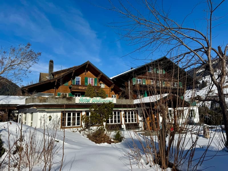 2 story hotel, wooden facade, green windows, snowy surroundings, mountain background