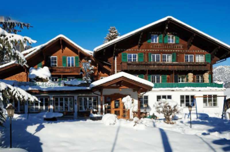 2 story brown wooden house, green windows, snow covered, balcony on the first floor