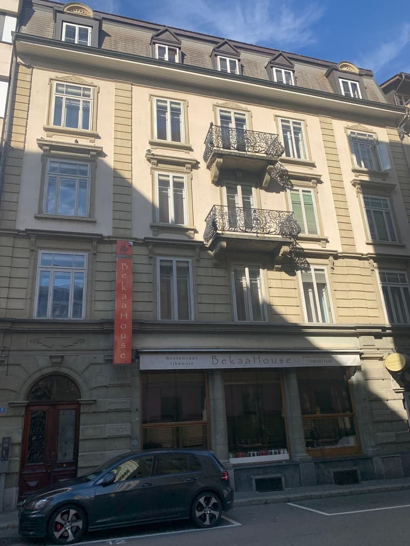 The building has two floors with balconies, a red sign indicating it is named 'BekaaHouse', and two windows on each floor with an additional window at the top.