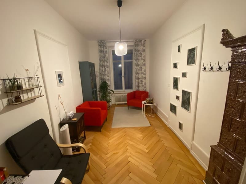 large room, wooden floor, white walls, 2 red armchairs, white rug, white curtains, picture frame wall, side table, shelving with plants