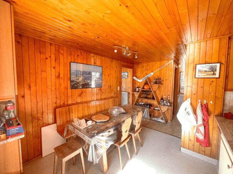 Dining room with wooden walls, dining table, chairs, wooden shelves, framed pictures, hockey stick, bottles, radiator, towels