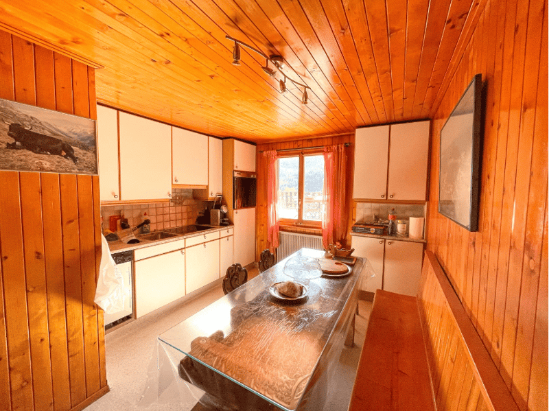 kitchen with dining area, wooden walls, glass table, white cabinets, sink, dishwasher, window with curtains