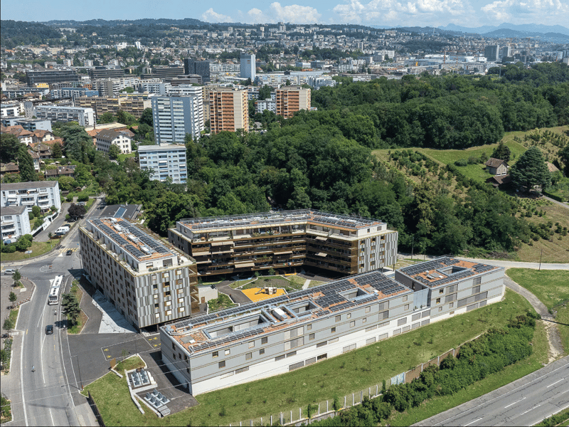 modern building, multiple floors, solar panels on rooftop, surrounding greenery, playground