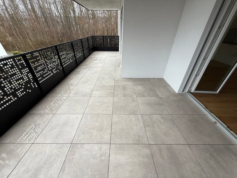Balcony with tiled floor, black railing, glass door, view of trees