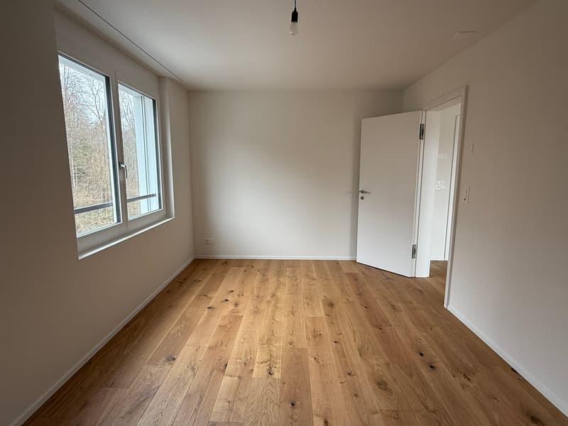 Empty room with hardwood floors, white walls, large windows, and an open door.