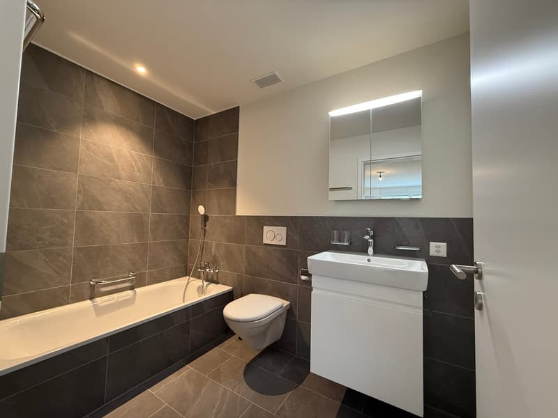 Bathroom with bathtub, toilet, sink, mirror, and tiled walls and floor