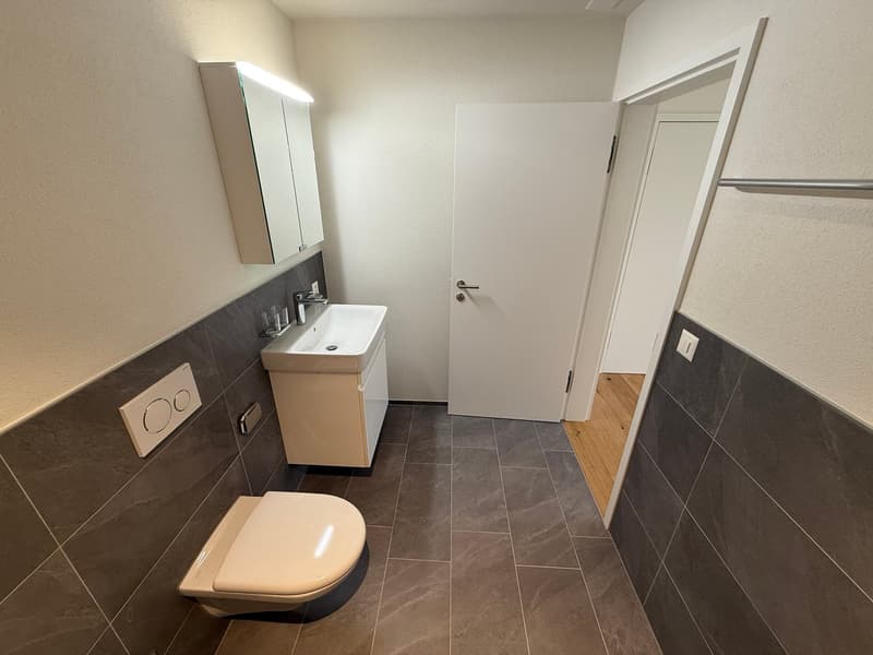 Bathroom with white toilet, sink, mirror, and tiled floor