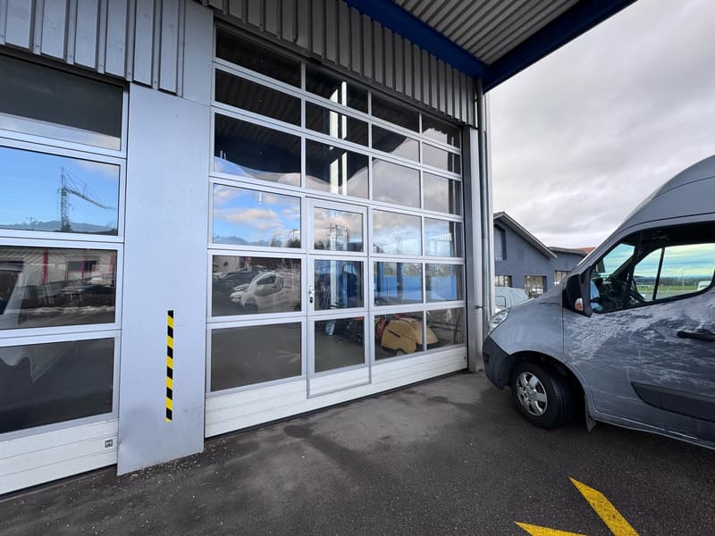 A commercial building with a large roll-up door, large windows and an empty parking lot in front of it. A van is parked nearby.