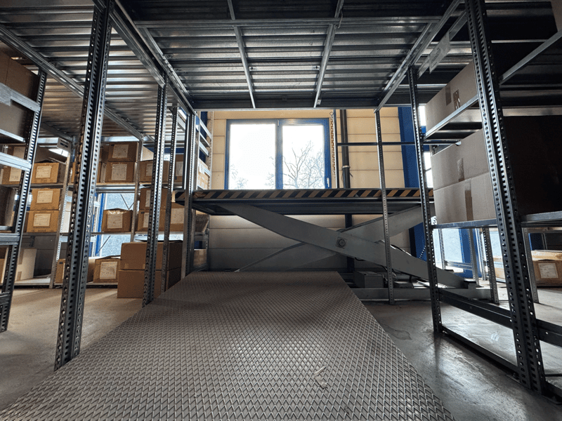 large warehouse with metal shelves, metal floor, metal ramp, metal staircase, window